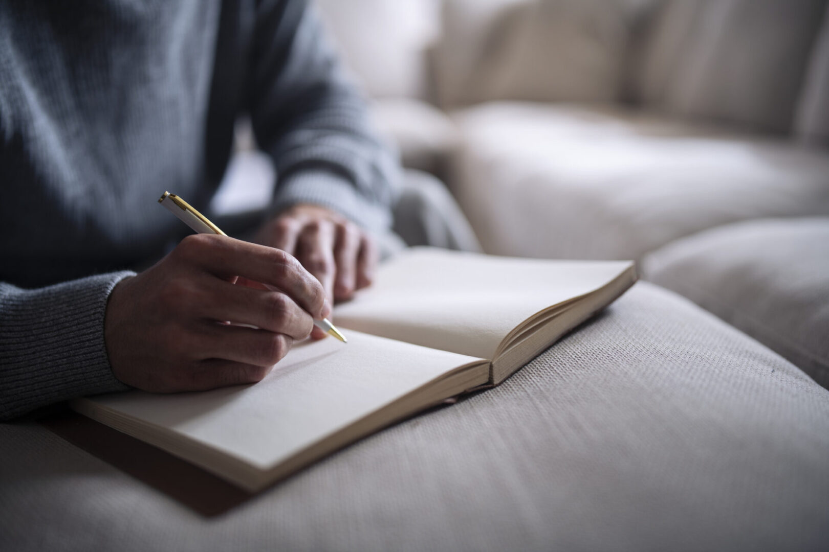 Person writing in a notebook on couch.