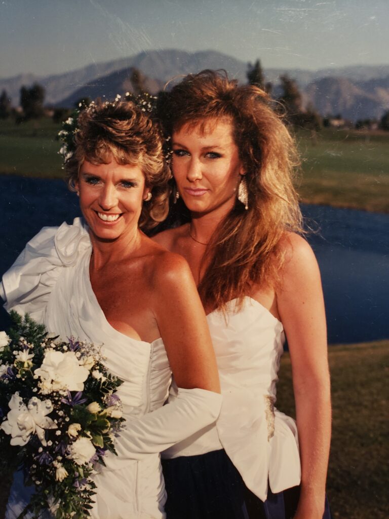 Two women in white wedding dresses posing outdoors
