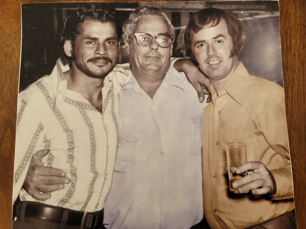 Three men smiling, one holding a drink