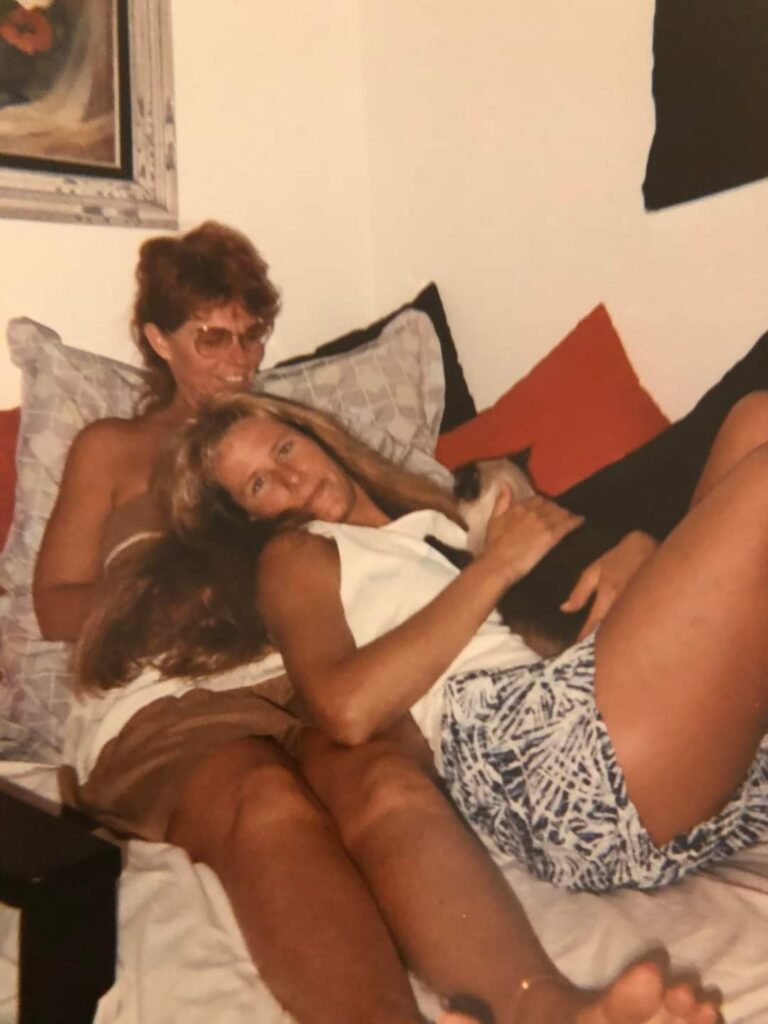 Two women lounging on bed with cat