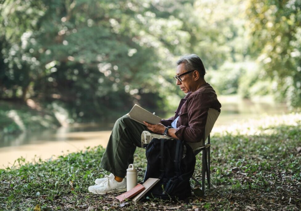 Man reading by a riverside in nature.