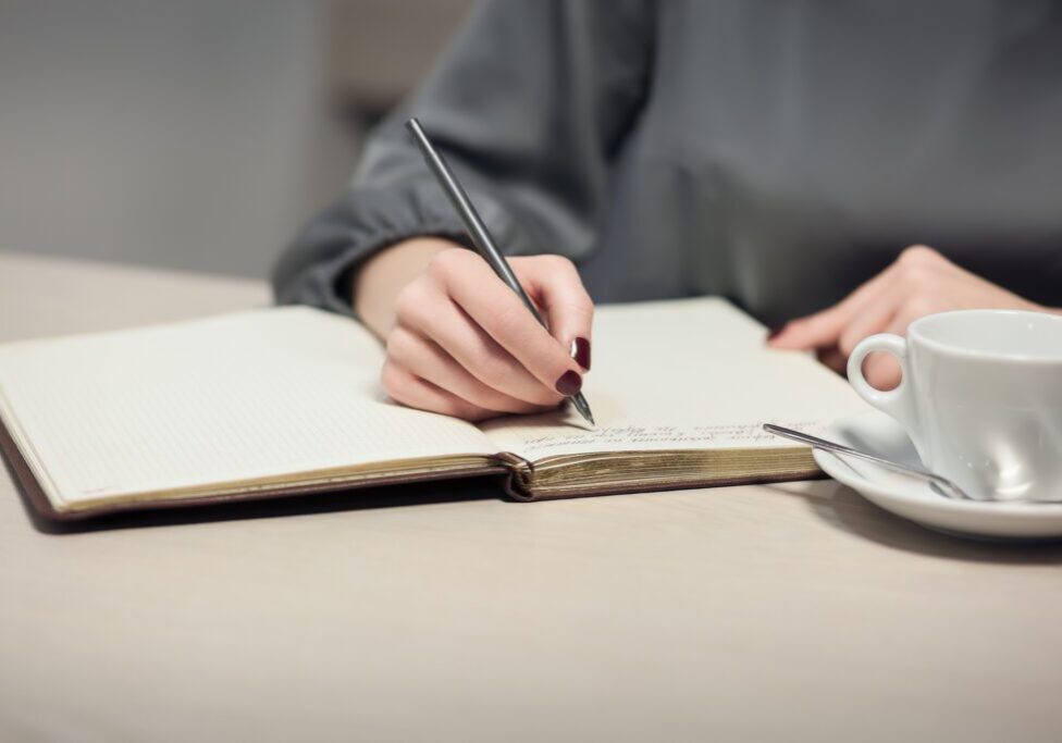 woman has a cup of tea and making notes in notepad; writer makes a novel; poet writes a poem;