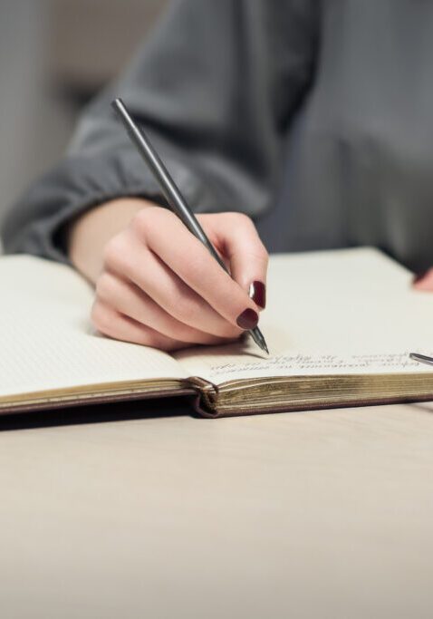 Hand writing in notebook beside coffee cup