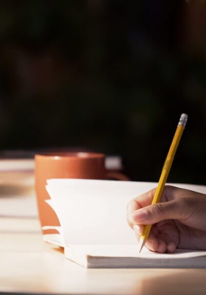 Hand writing in notebook near lamp