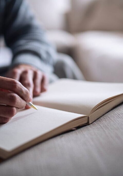 Person writing in open notebook on couch