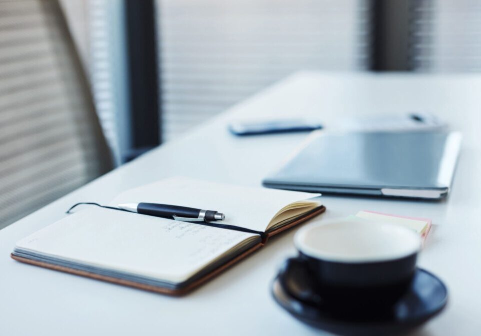 Notebook, pen, and coffee cup on desk.