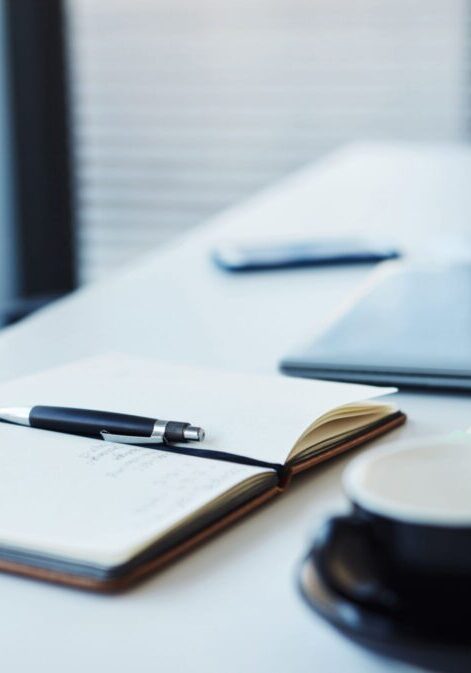 Notebook, pen, and coffee cup on desk.